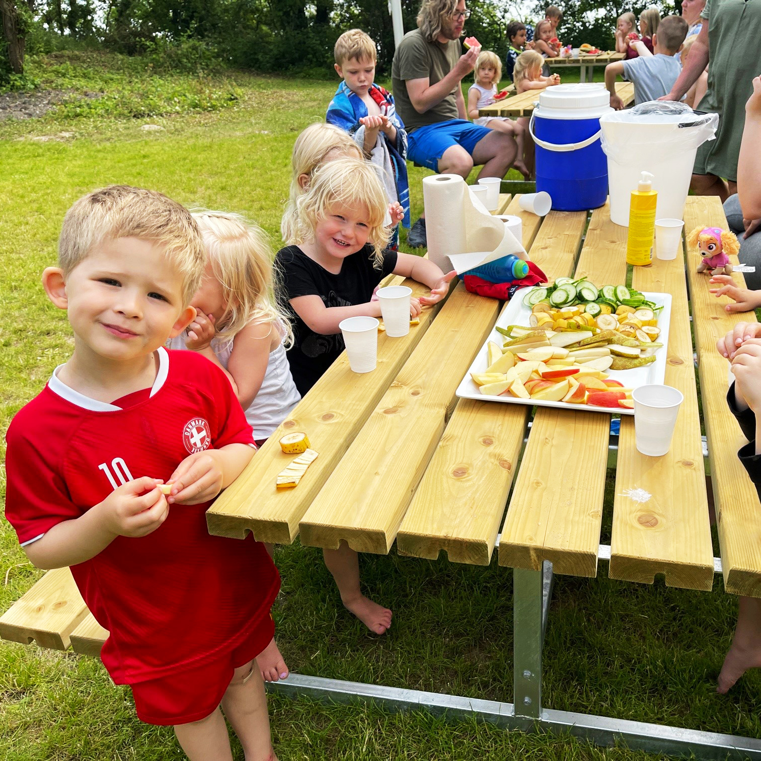 Glade børn der spiser ved de udendørs borde og bænke